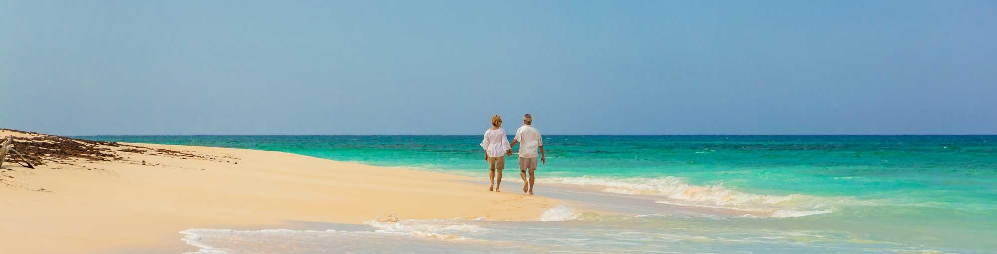 An elderly couple walking hand-in-hand on a sunny beach